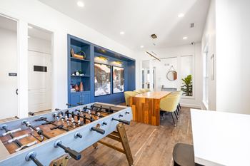 A foosball table is in the middle of a room with a blue cabinet and a wooden table.